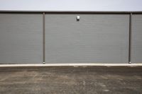 gray building with three closed doors next to it on a road side, outside of which is an empty lot