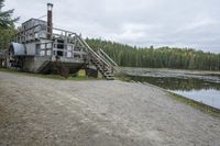 a rustic log house sitting next to a lake and forest area with steps leading to the house