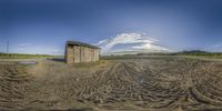 an outhouse stands in a muddy field, with a sky background behind it on a partly cloudy day