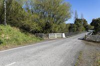 a gate sits on the side of a road next to a wooded area with grass and plants