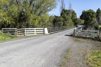 a gate sits on the side of a road next to a wooded area with grass and plants