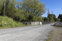 a gate sits on the side of a road next to a wooded area with grass and plants