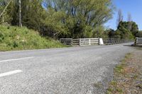 a gate sits on the side of a road next to a wooded area with grass and plants