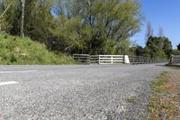 a gate sits on the side of a road next to a wooded area with grass and plants