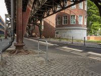 the train station has a rusted steel structure on it's side, with buildings lining the track, along with a brick road and sidewalk