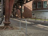 the train station has a rusted steel structure on it's side, with buildings lining the track, along with a brick road and sidewalk