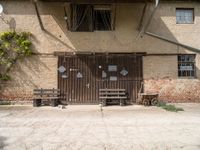 a rustic, wooden structure in front of a brick wall and entrance with two wooden benches