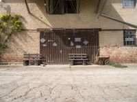 a rustic, wooden structure in front of a brick wall and entrance with two wooden benches