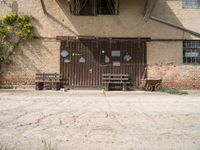 a rustic, wooden structure in front of a brick wall and entrance with two wooden benches