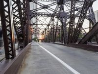 a pedestrian is crossing a rusty bridge with a view of buildings in the distance on a late evening