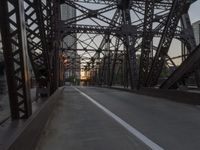 a pedestrian is crossing a rusty bridge with a view of buildings in the distance on a late evening