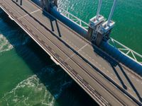 a truck crossing a bridge over the ocean near some pipes and smoke stacks above it