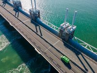 a truck crossing a bridge over the ocean near some pipes and smoke stacks above it