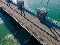 a truck crossing a bridge over the ocean near some pipes and smoke stacks above it