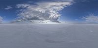 a snow covered field with many clouds behind it with the sun in the sky above