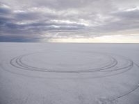 a circle shaped picture with clouds in the background on a desert plain with footprints in the sand