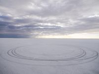 a circle shaped picture with clouds in the background on a desert plain with footprints in the sand