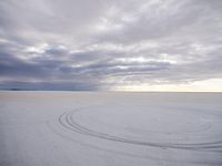 a circle shaped picture with clouds in the background on a desert plain with footprints in the sand