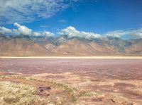 a dry lake with mud on it surrounded by mountains in the distance there is pink salt floating off the ground
