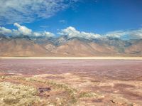 a dry lake with mud on it surrounded by mountains in the distance there is pink salt floating off the ground