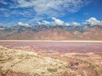 a dry lake with mud on it surrounded by mountains in the distance there is pink salt floating off the ground