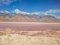 a dry lake with mud on it surrounded by mountains in the distance there is pink salt floating off the ground