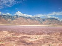 a dry lake with mud on it surrounded by mountains in the distance there is pink salt floating off the ground