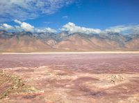 a dry lake with mud on it surrounded by mountains in the distance there is pink salt floating off the ground