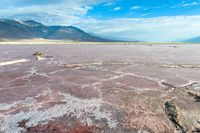 a sandy plain with an unusual sky background and mountains in the background the colors of the mud and the rocks