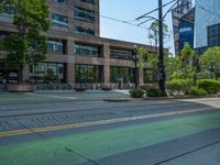 the green paint is painted on a bike path in front of an office building and large, trees