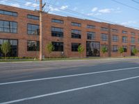 an empty street in front of a large red brick building on the other side of the road is a street light that has a line for motorists