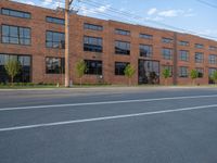 an empty street in front of a large red brick building on the other side of the road is a street light that has a line for motorists