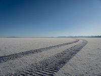 the tire tracks are visible in the sand of the barren landscape against a blue sky