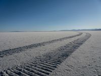 the tire tracks are visible in the sand of the barren landscape against a blue sky