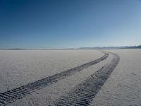 the tire tracks are visible in the sand of the barren landscape against a blue sky