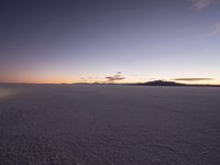 a motorcycle parked in a deserted, flat area at sunset with a sky background and mountains in the distance