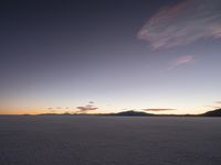 a motorcycle parked in a deserted, flat area at sunset with a sky background and mountains in the distance