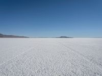 tire tracks in an expanse with mountain ranges in the distance of a vast plain plain