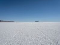 tire tracks in an expanse with mountain ranges in the distance of a vast plain plain