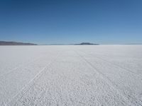 tire tracks in an expanse with mountain ranges in the distance of a vast plain plain