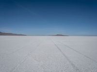 tire tracks in an expanse with mountain ranges in the distance of a vast plain plain