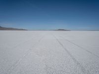 tire tracks in an expanse with mountain ranges in the distance of a vast plain plain