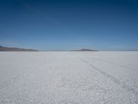 tire tracks in an expanse with mountain ranges in the distance of a vast plain plain