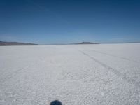 tire tracks in an expanse with mountain ranges in the distance of a vast plain plain