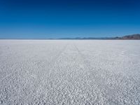 a vast plain covered in white snow with mountains in the background, with tracks that cross between them