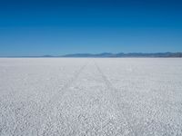 a vast plain covered in white snow with mountains in the background, with tracks that cross between them