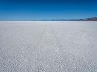 a vast plain covered in white snow with mountains in the background, with tracks that cross between them