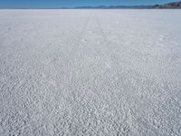 a vast plain covered in white snow with mountains in the background, with tracks that cross between them