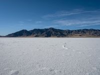 an empty area with a mountain in the distance and some footprints in the sand on it