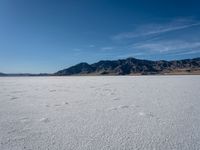 an empty area with a mountain in the distance and some footprints in the sand on it